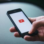 Close-up of a hand holding a smartphone displaying the YouTube app on the screen.